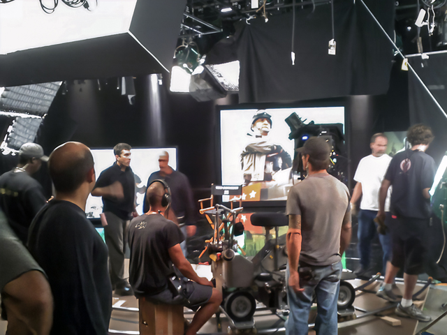 Behind-the-scenes view of a Fox Studios set, with crew members, cameras, lighting rigs, monitors, and production equipment surrounding the filming area.