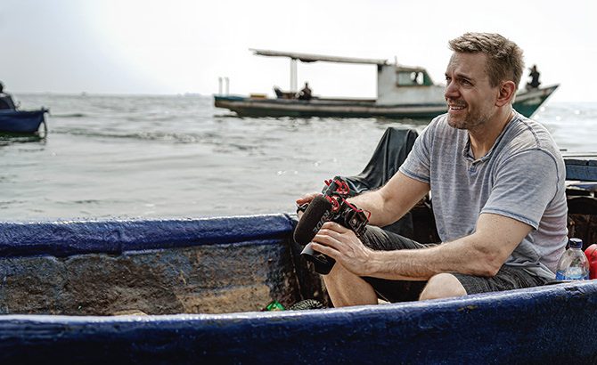 Brian Dickett seated in a blue fishing boat during an outdoor production shoot.
