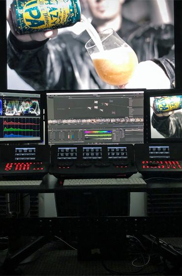 Professional video editing workstation with multiple monitors showing a Sierra Nevada Hazy IPA commercial, color grading scopes, timeline controls, and a large preview of a drink being poured.