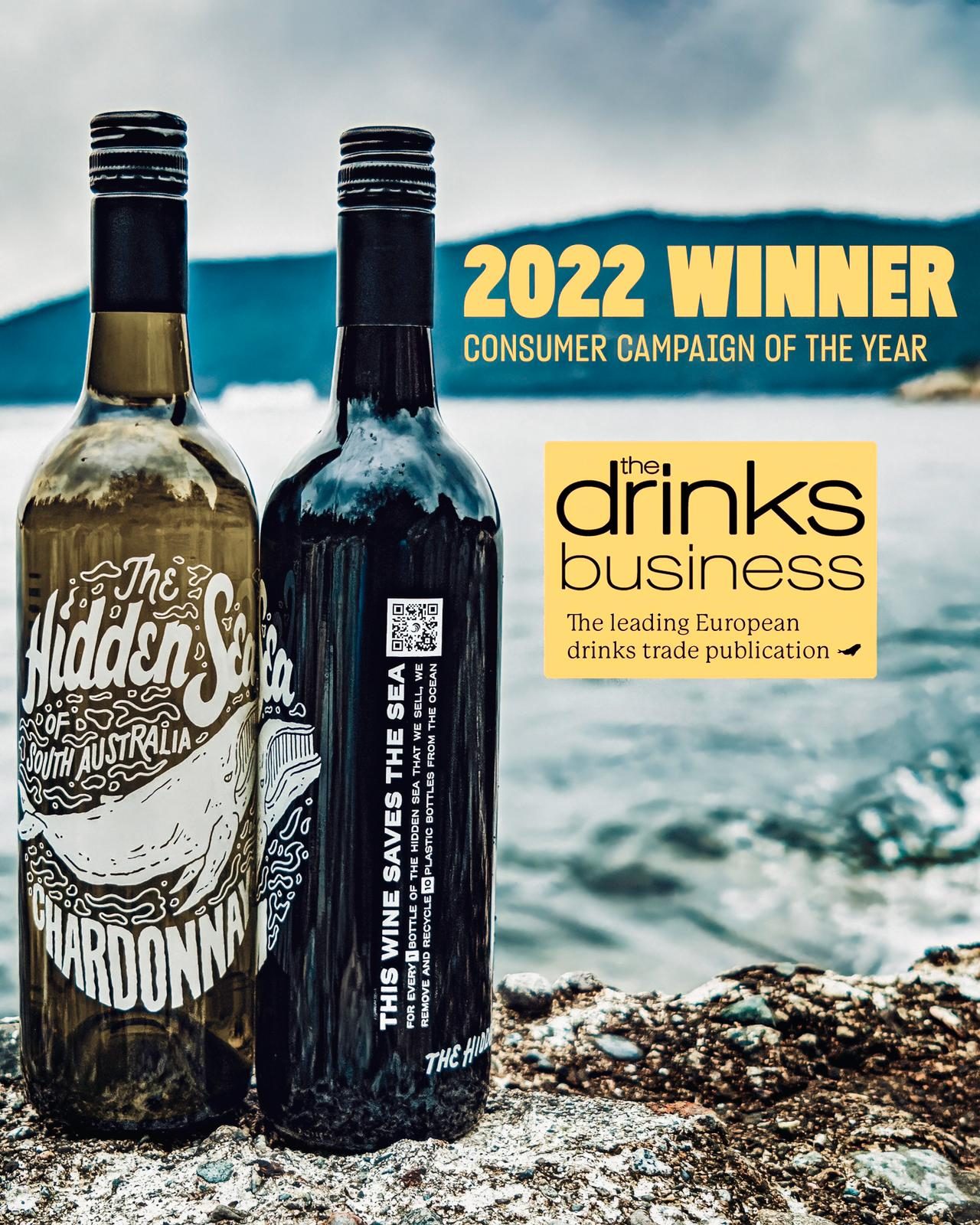 Two bottles of The Hidden Sea wine stand on a rocky shoreline beside the water, with mountains in the background. Text reads, “2022 Winner, Consumer Campaign of the Year,” alongside The Drinks Business logo.